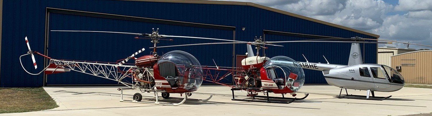 Three helicopters parked in front of a blue hangar on a sunny day.