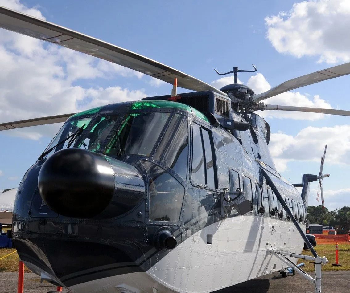 A dark blue and silver helicopter with large blades, sitting outdoors on a sunny day.