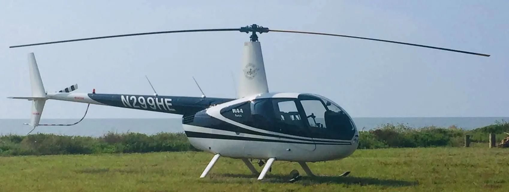 A helicopter on grass near the ocean, with the blades extended. It is painted white and dark blue.