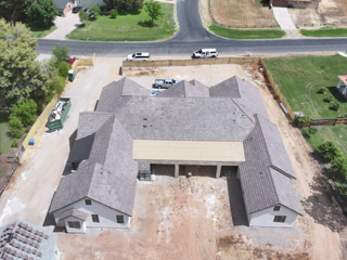 Aerial view of a large gray-roofed house under construction with vehicles and dirt surrounding it.