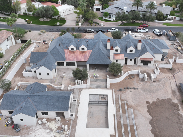 Aerial view of a large gray-roofed house under construction with a central courtyard and unfinished landscaping
