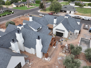 Aerial view of a house under renovation with gray roofs, white walls, and construction materials in the yard.