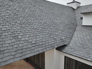 Gray shingled roof with multiple slopes and a small dormer window on a building