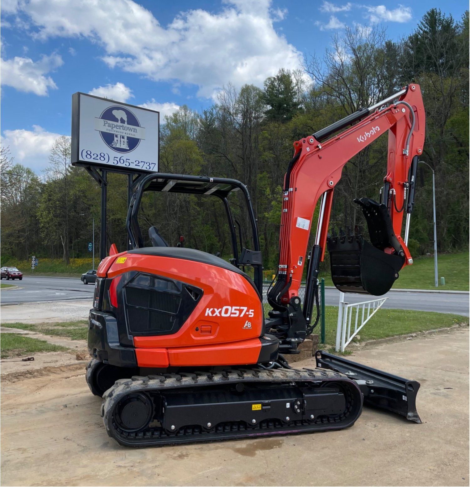 Orange Kubota KX057-5 mini excavator on display outside a business with a sign.