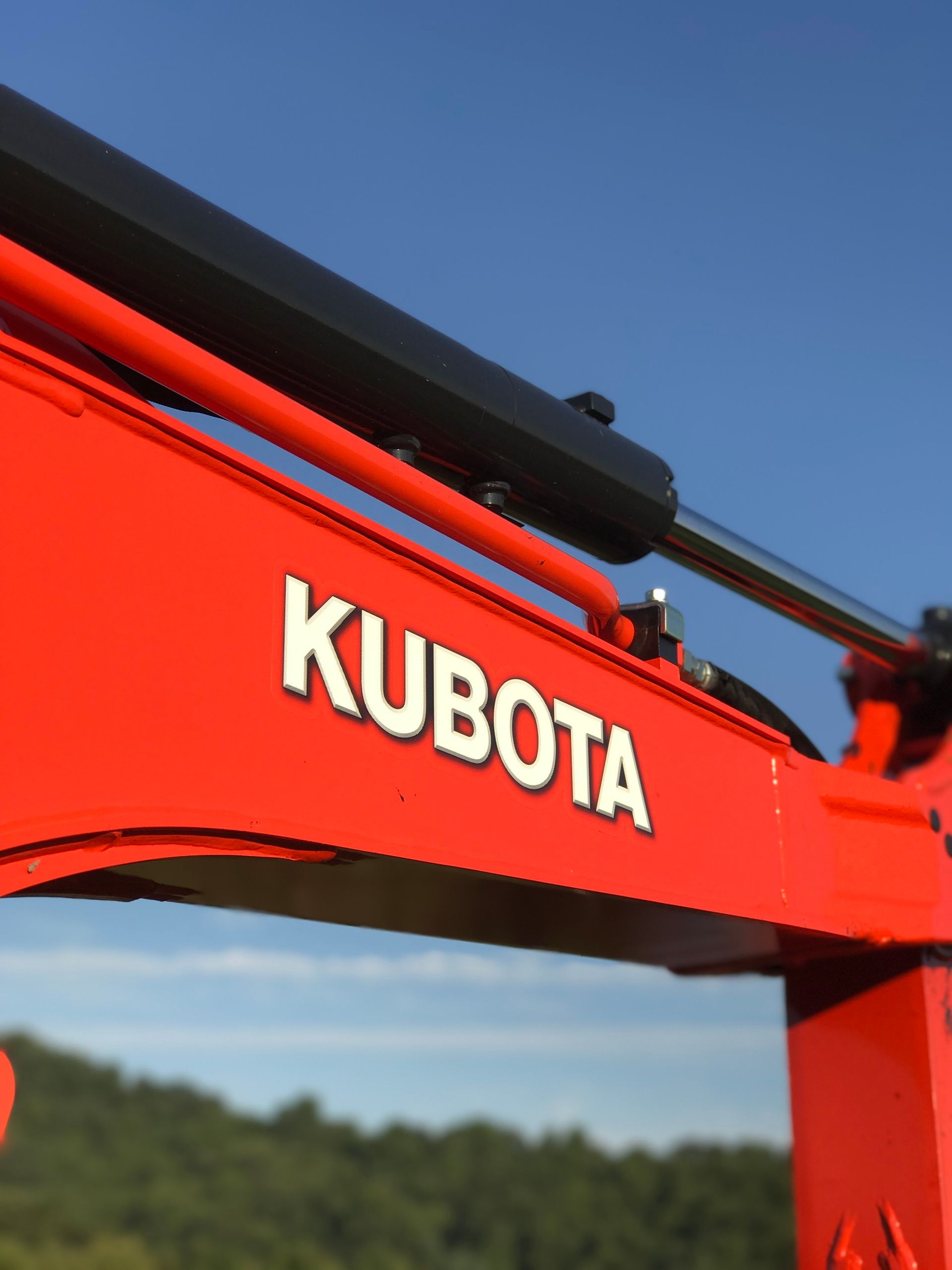 Orange Kubota excavator arm with white logo against blue sky.
