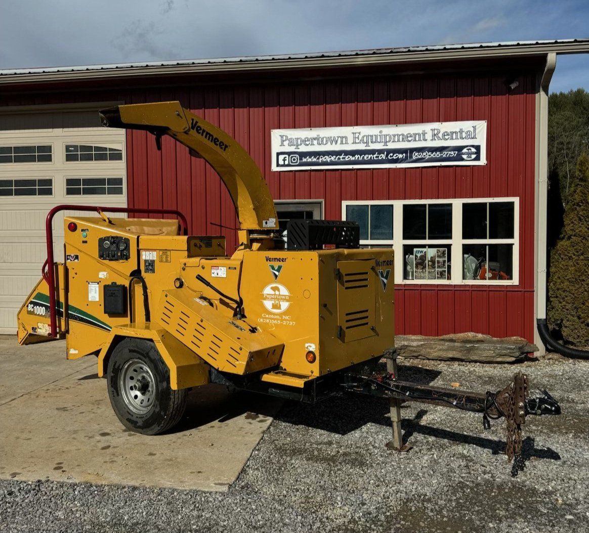 Yellow wood chipper on trailer parked in front of red building with rental sign.