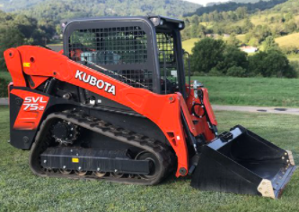 Orange Kubota SVL75 track skid steer loader with bucket on grass, mountains in background.