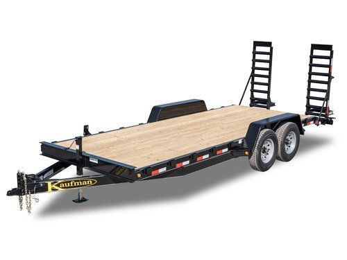 Black and tan Kaufman Equipment trailer with two ramps and dual wheels.