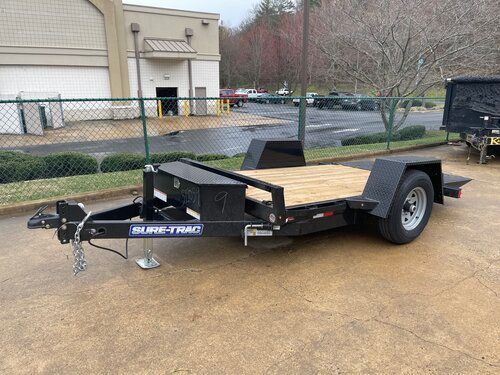 Black SURF TRAC utility trailer parked on concrete with a wooden deck and black storage box.