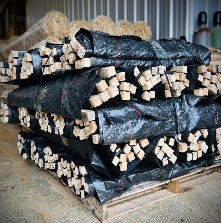 Bundled wooden stakes wrapped in black material stacked on a wooden pallet in a warehouse.