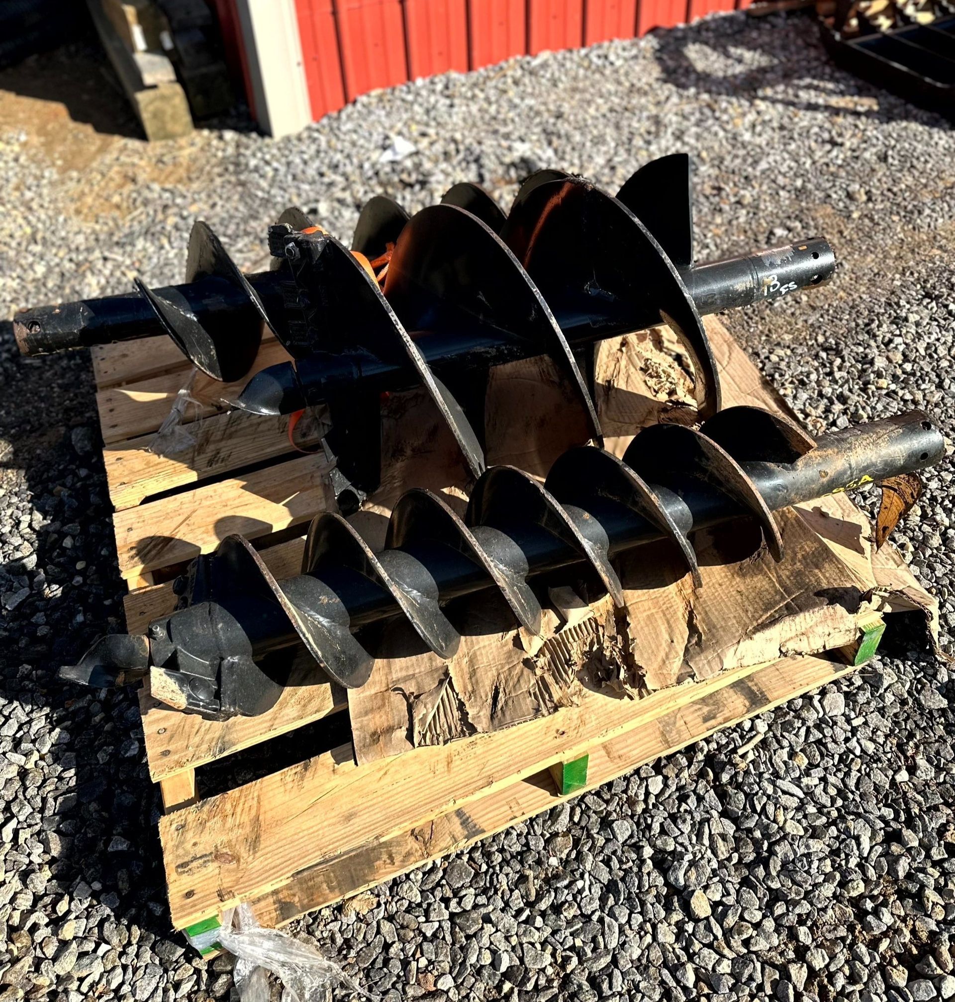 Black auger drill bits on a wooden pallet, outdoors.