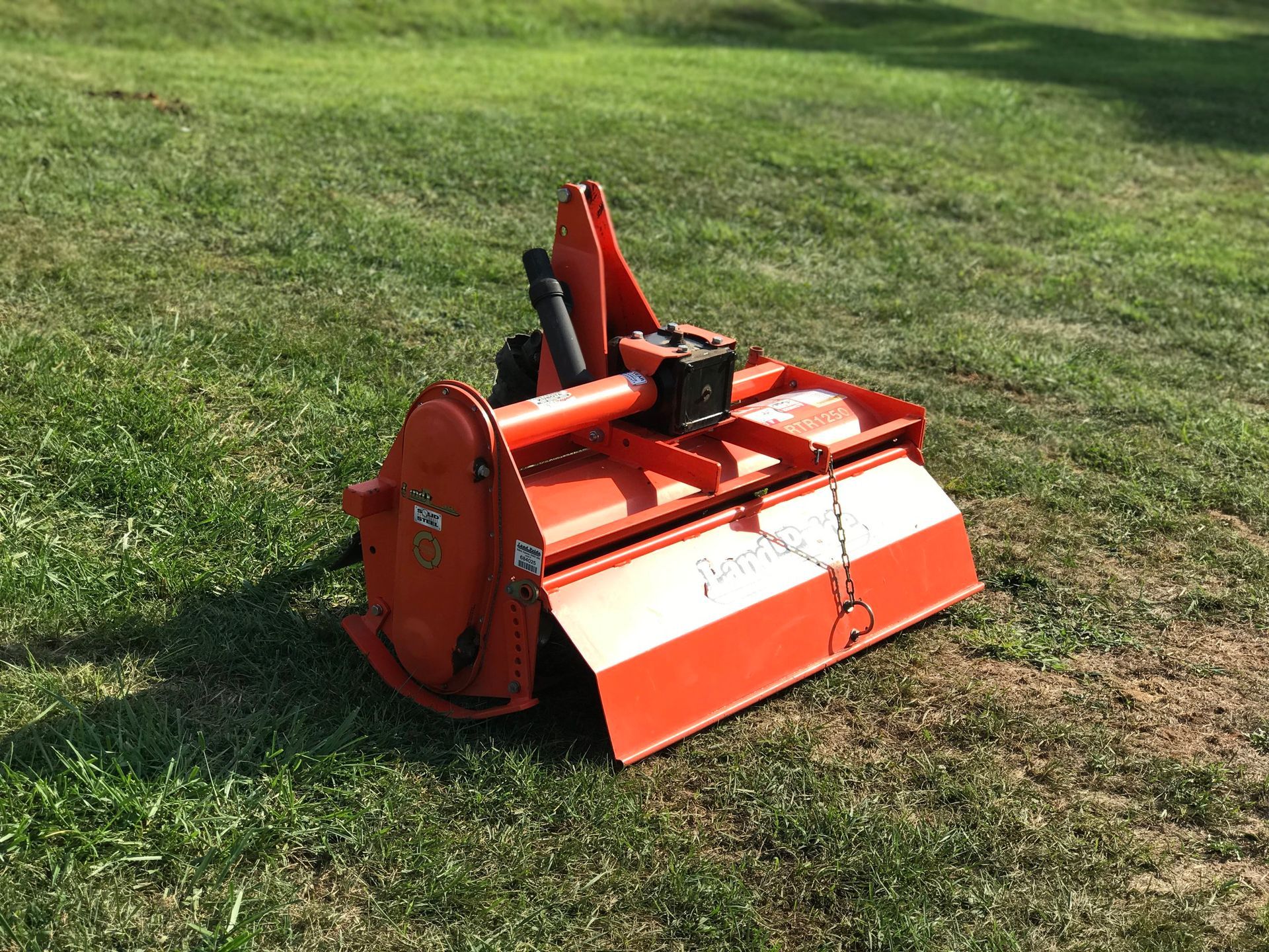 Orange rotary tiller on green grass, likely used for gardening or agriculture.