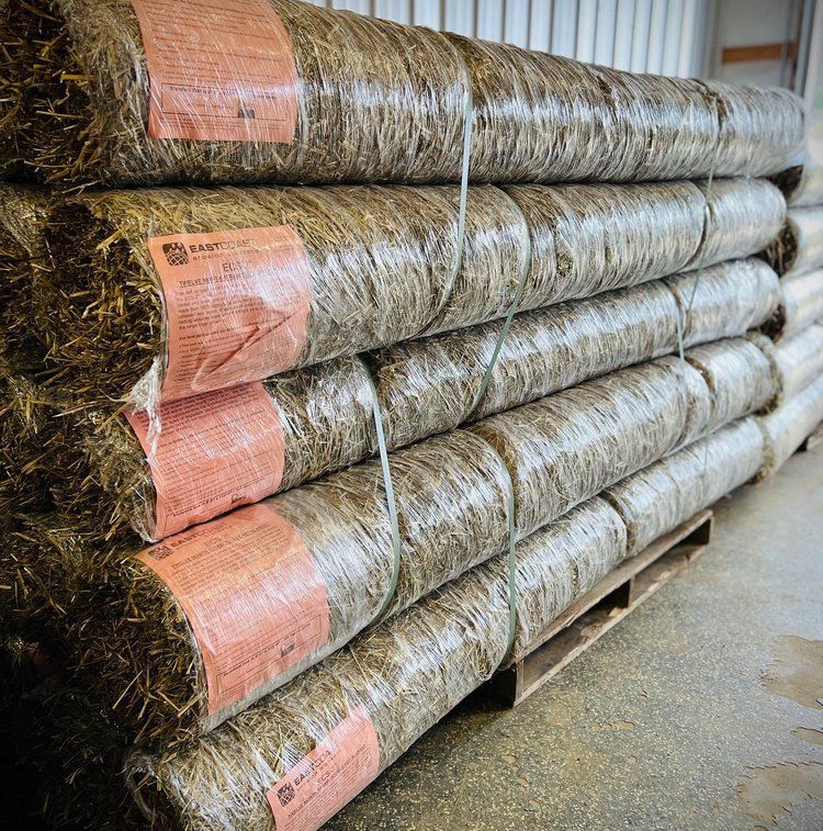 A stack of rolled-up hay bales wrapped in plastic, with labels visible.