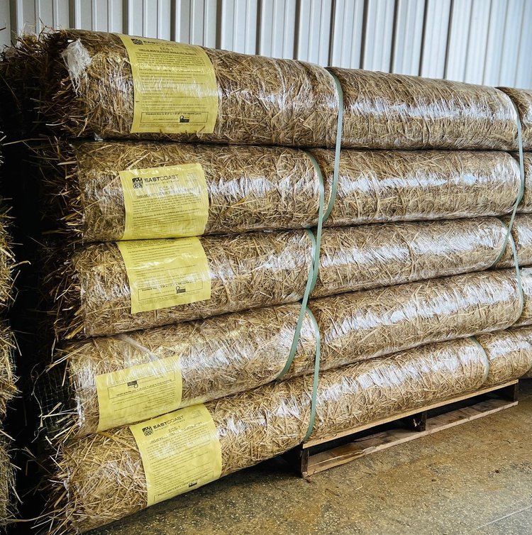 Stacked rolls of straw wrapped in plastic on a wooden pallet; intended for erosion control.