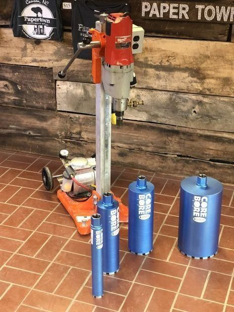 Core drill machine with multiple blue core bits on a brick floor.