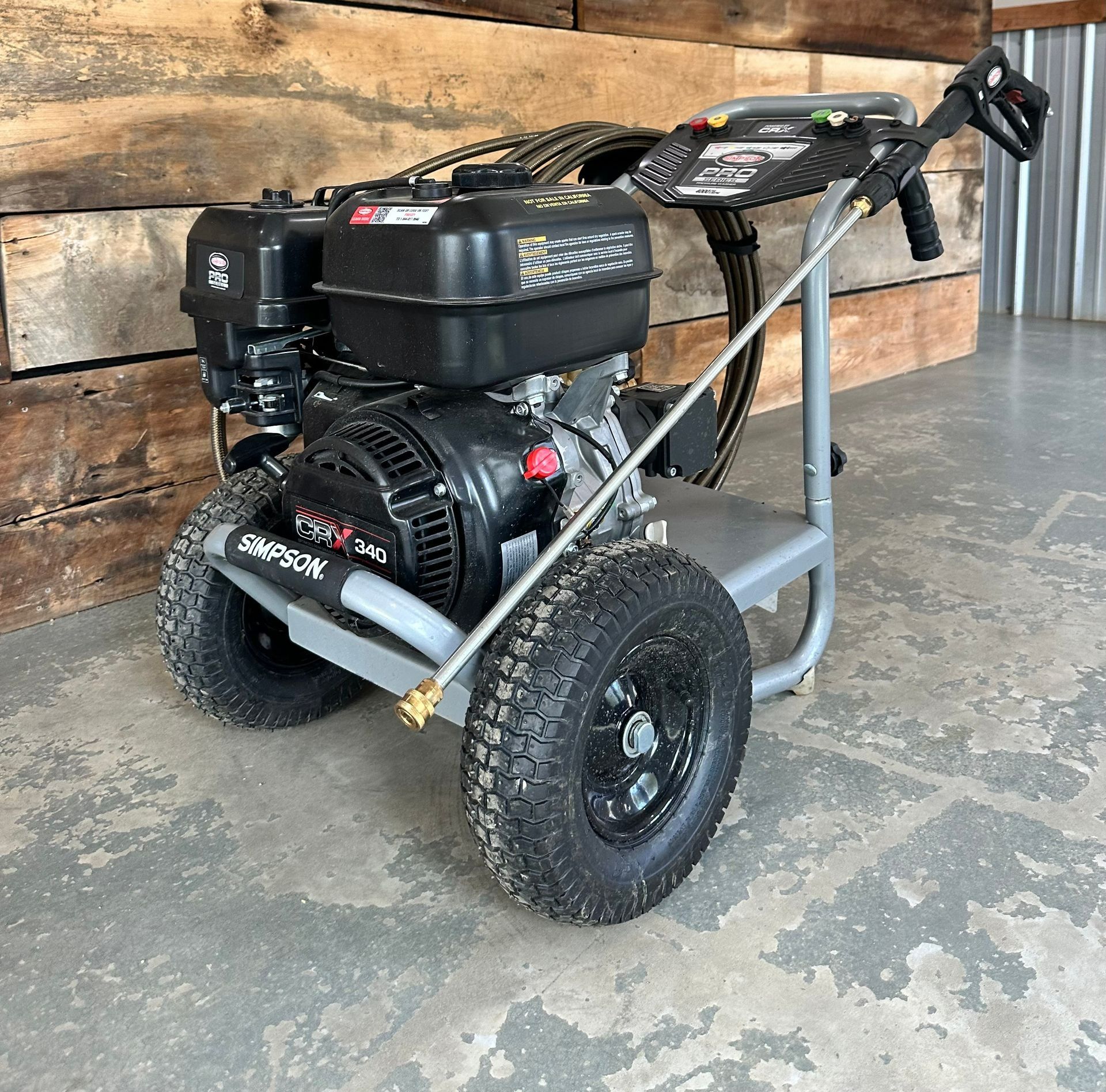 Simpson pressure washer with black wheels, engine, and hose on a concrete surface.