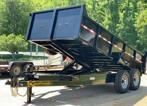 Black dump trailer with the bed raised, hitched to a tow vehicle, outdoors.