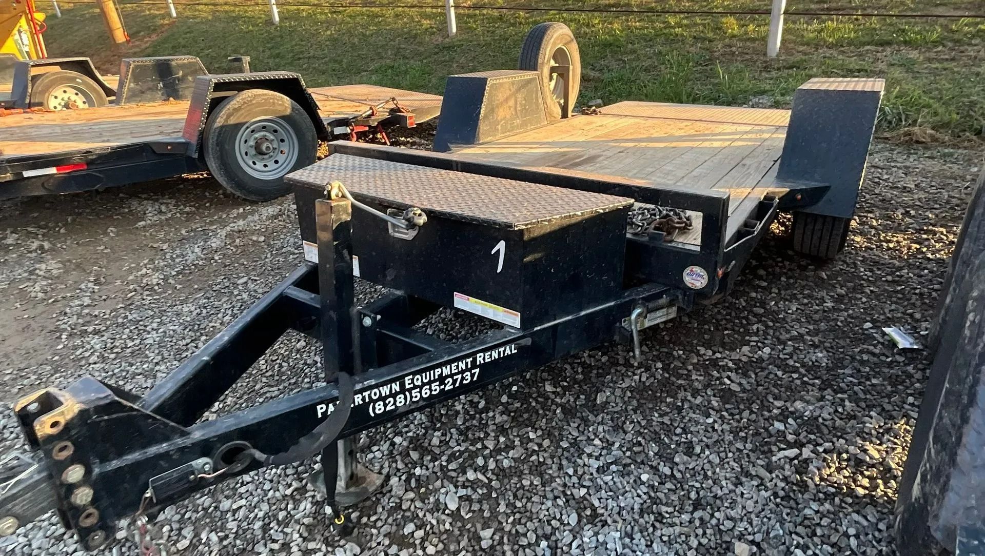 Black flatbed trailer with a spare tire, on a gravel lot.