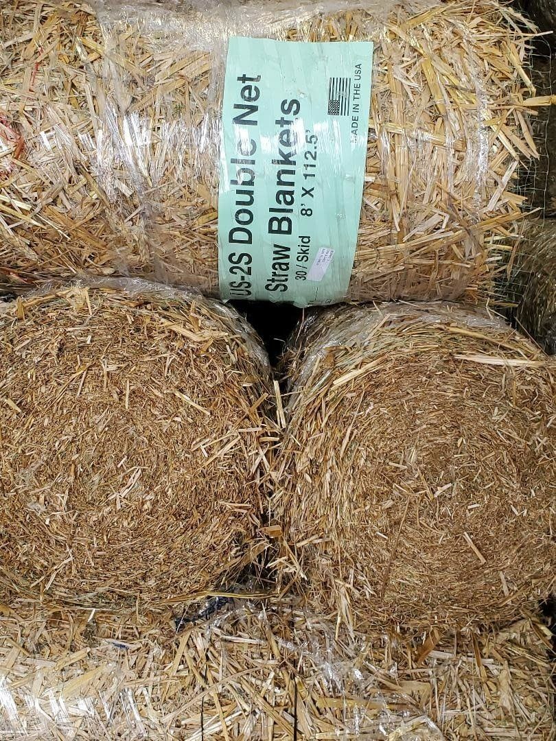 Stack of straw blankets wrapped in plastic, with a green label visible.