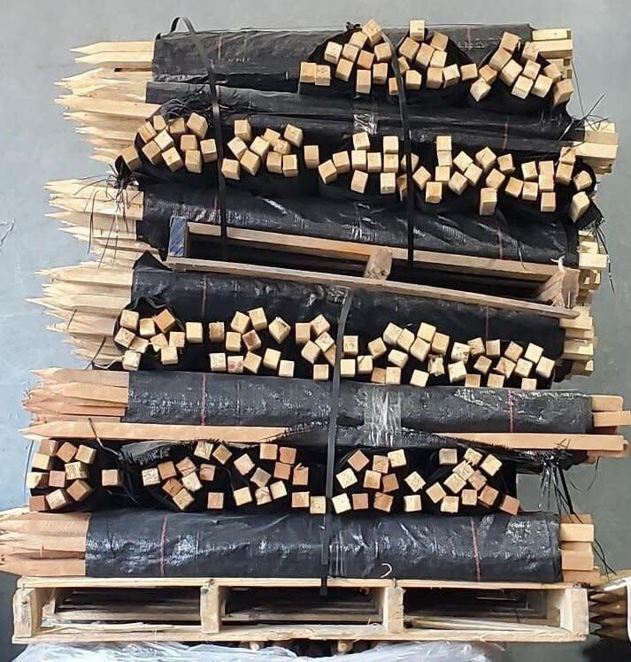 Wooden stakes and blocks bundled on pallets, wrapped in black plastic, stacked high.