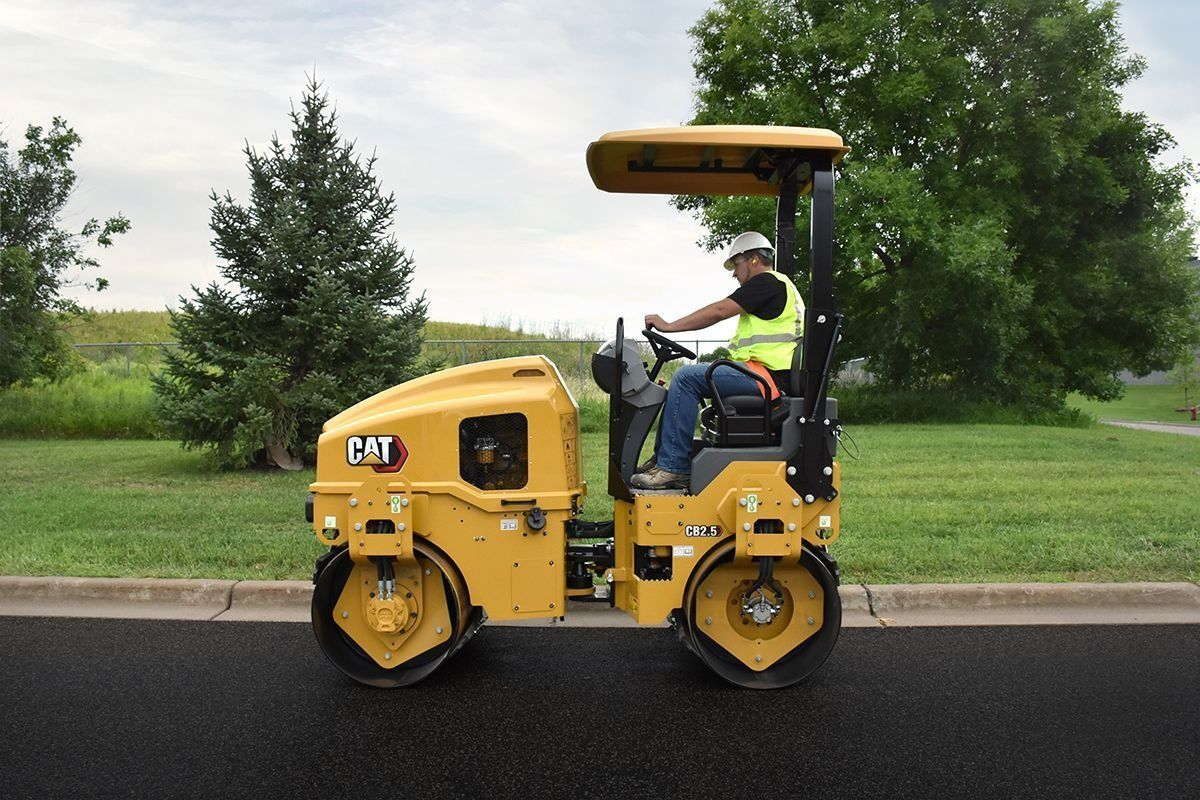 Yellow Caterpillar road roller compacting asphalt, operator wearing safety vest.