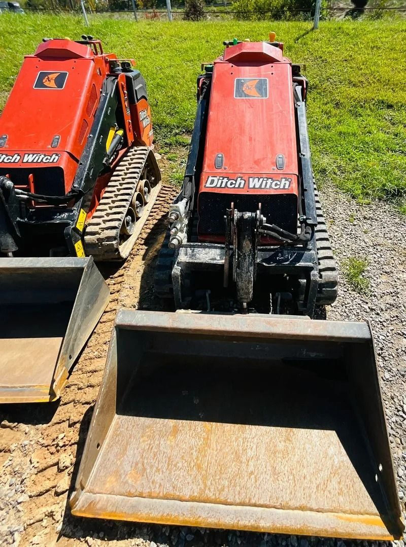 Two orange Ditch Witch mini skid steers with front buckets, outdoors.