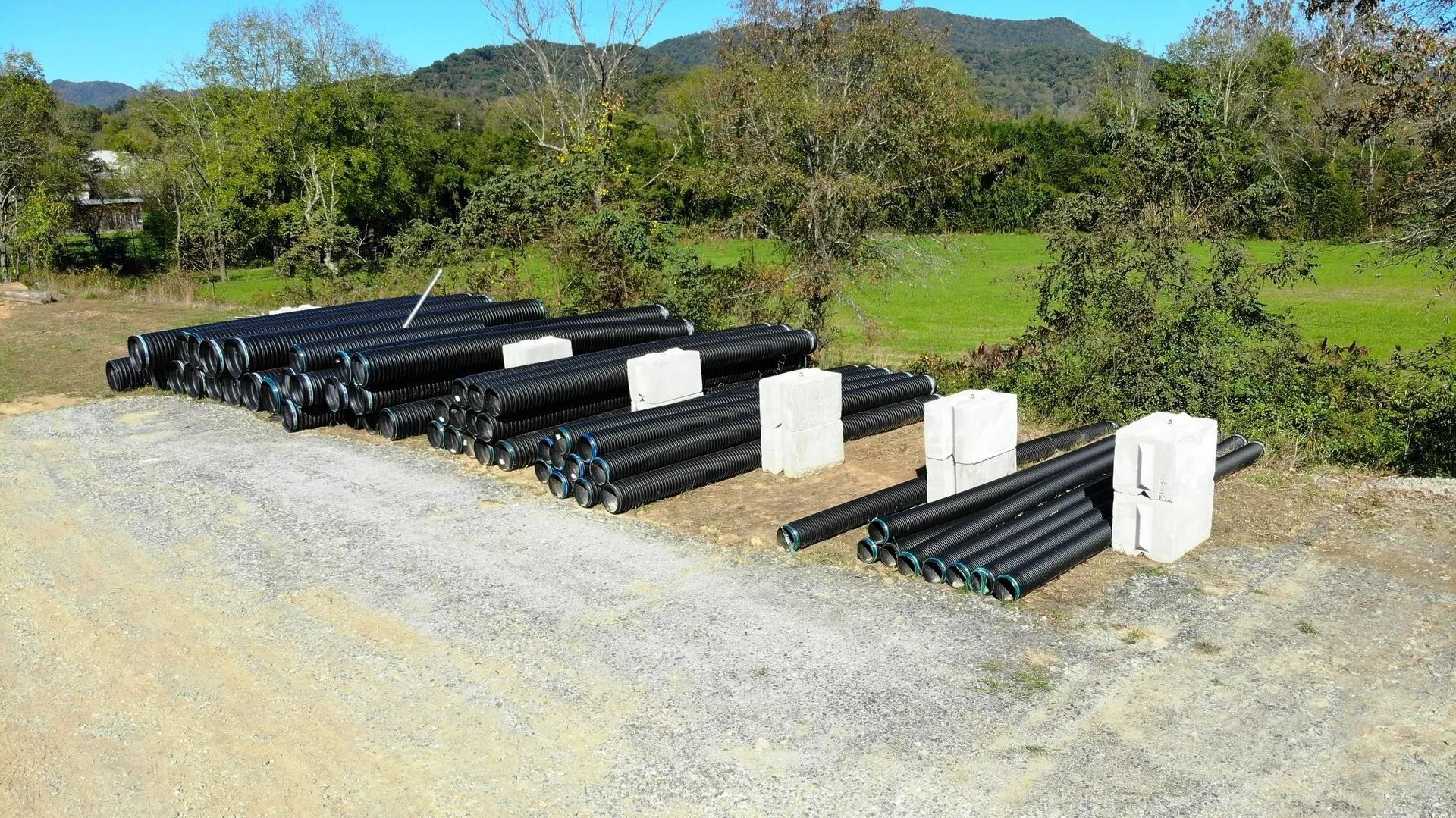 Black pipes and concrete blocks on gravel, with trees and hills in background.