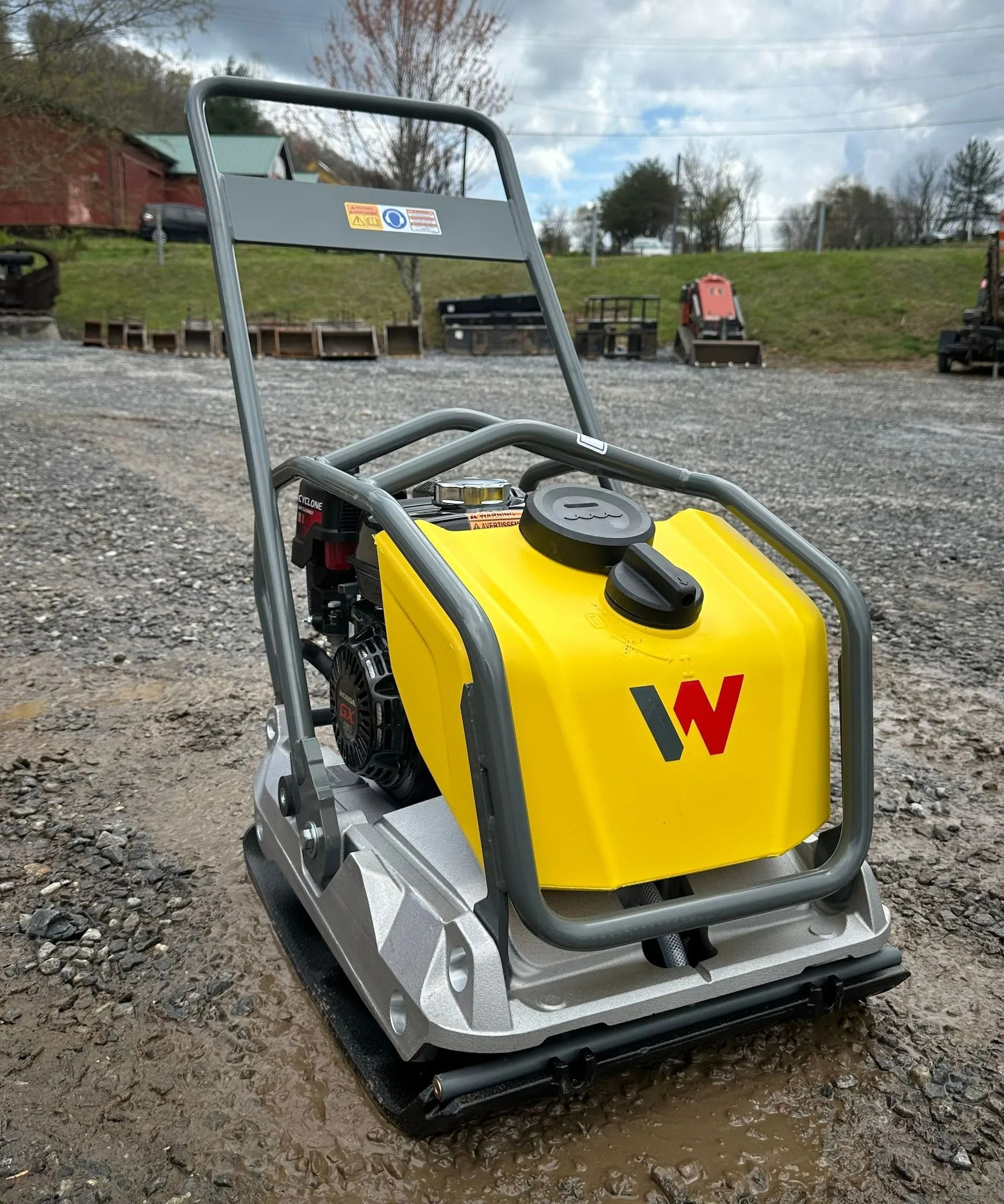 A yellow and gray Wacker Neuson plate compactor on a muddy surface.