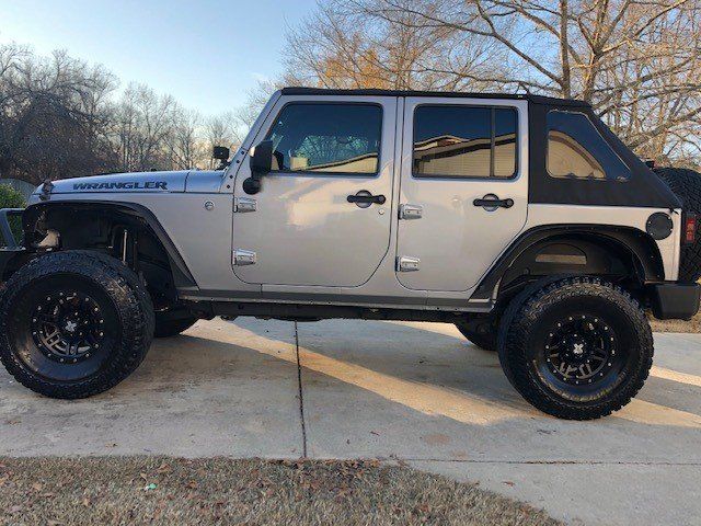 Silver Jeep Wrangler with black wheels parked on a paved driveway.