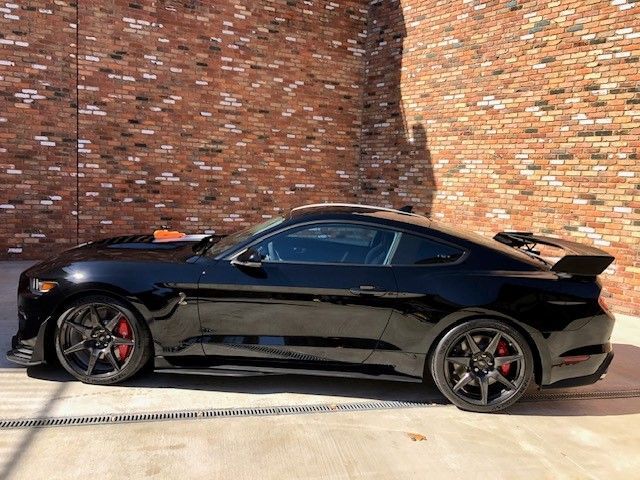 Black sports car with red brake calipers parked against a brick wall.