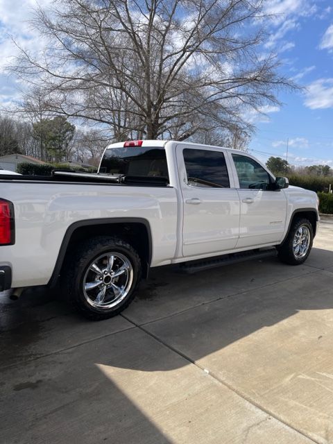 White pickup truck with chrome wheels parked on a concrete driveway, beneath a tree on a sunny day.