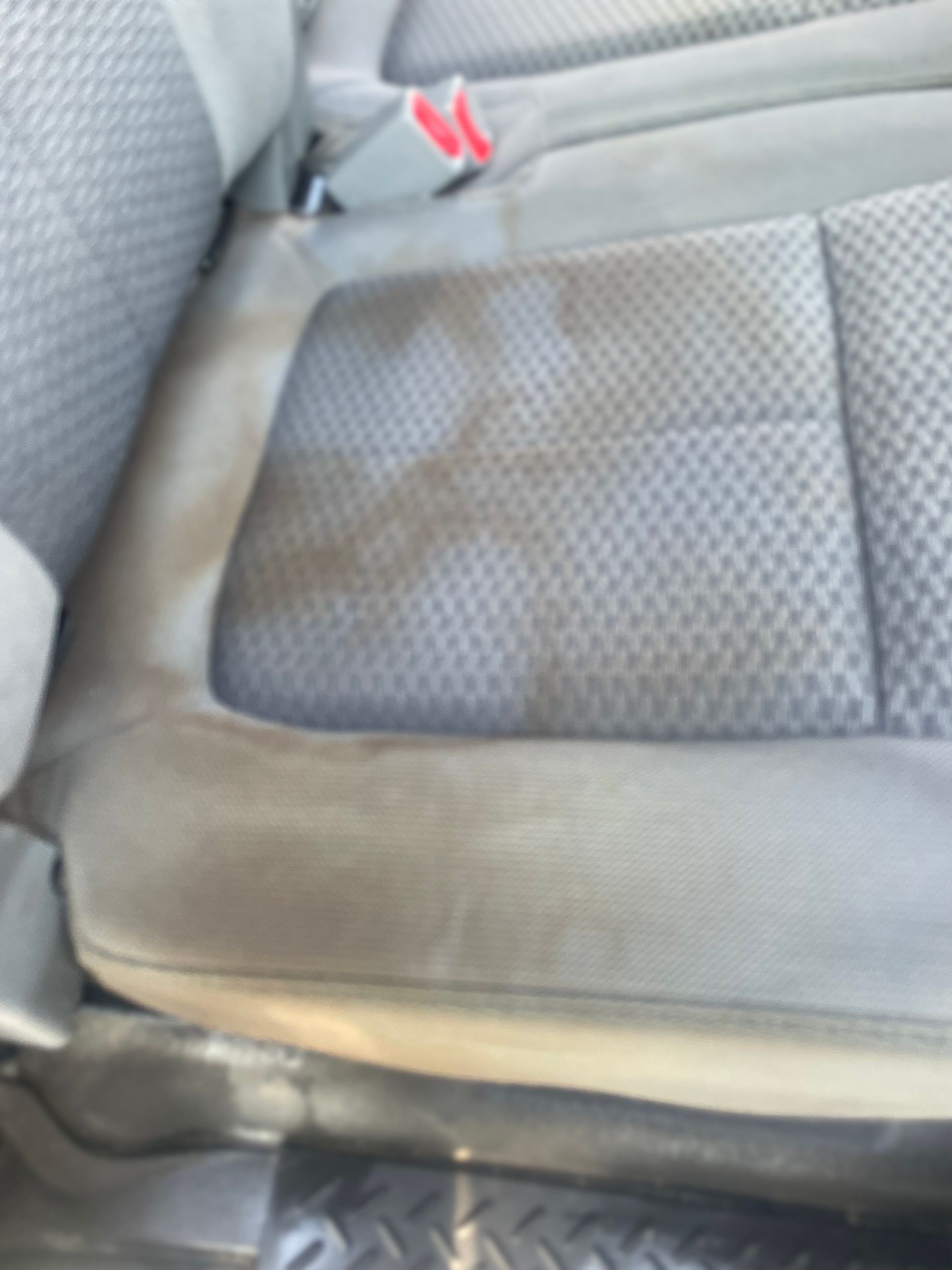 Gray fabric car seat showing a large, dark, irregular stain across the seat cushion and backrest.