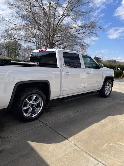 White pickup truck with chrome wheels parked on a driveway with a sunny sky in the background.