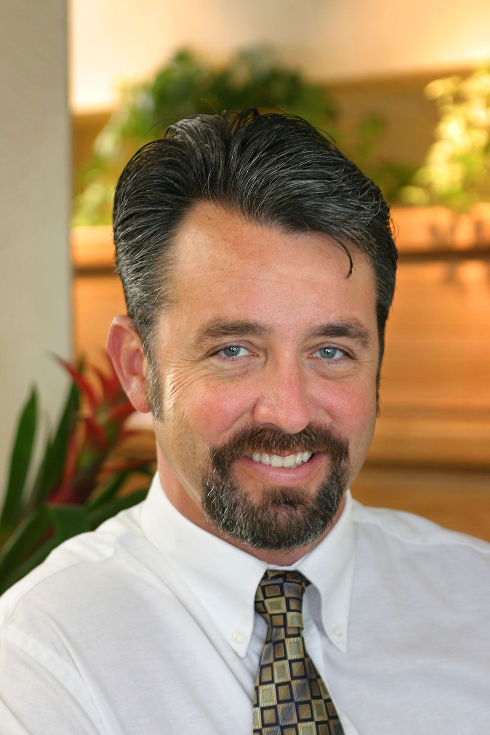 Smiling man in white shirt and patterned tie in a softly lit office setting