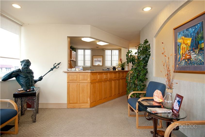Quiet waiting room with chairs, a reception desk, potted plant, and a small statue on a side table.