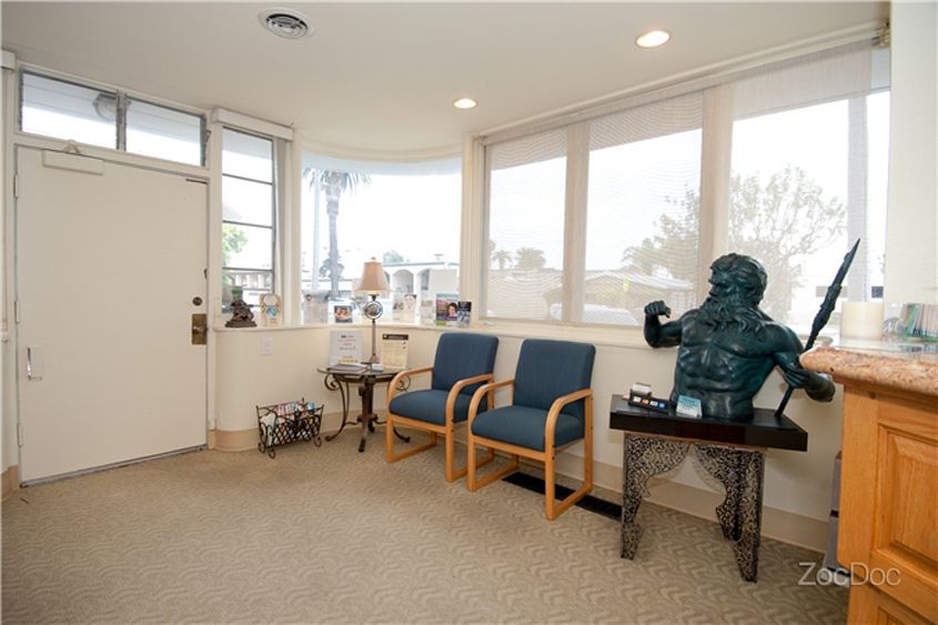 Bright waiting room with blue chairs, large windows, and a bust sculpture on a small table.