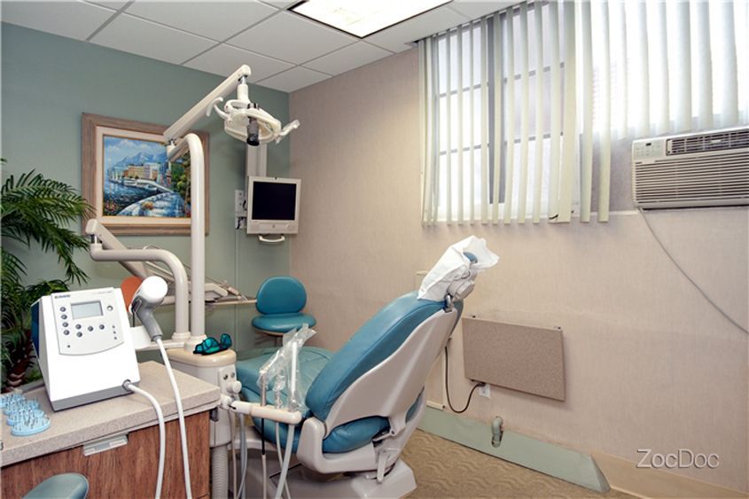 Dental exam room with blue chair, overhead light, and equipment on beige walls