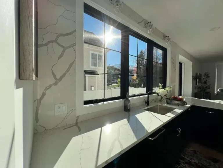 Bright modern kitchen with large windows, white countertops, and sunlight streaming in.
