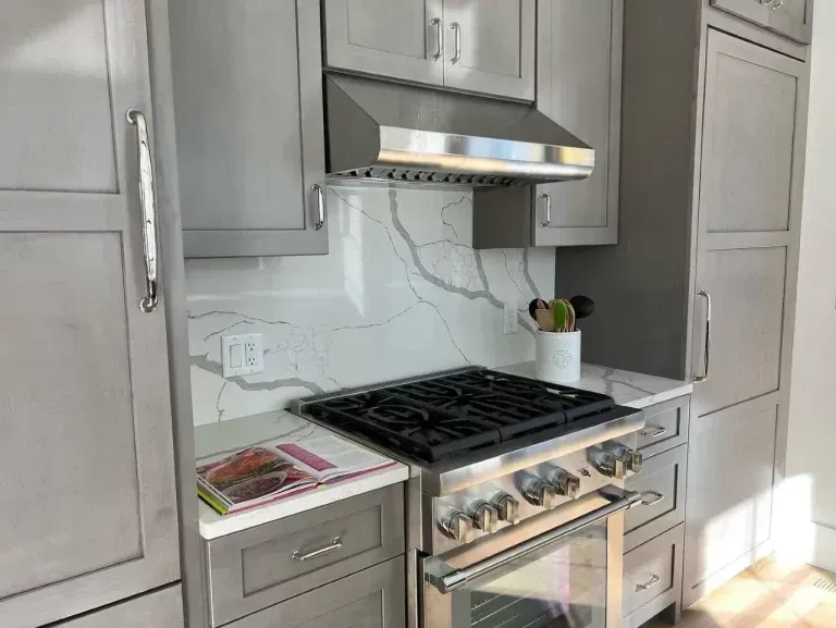 Modern kitchen with stainless steel stove, marble backsplash, white cabinets, and a range hood.