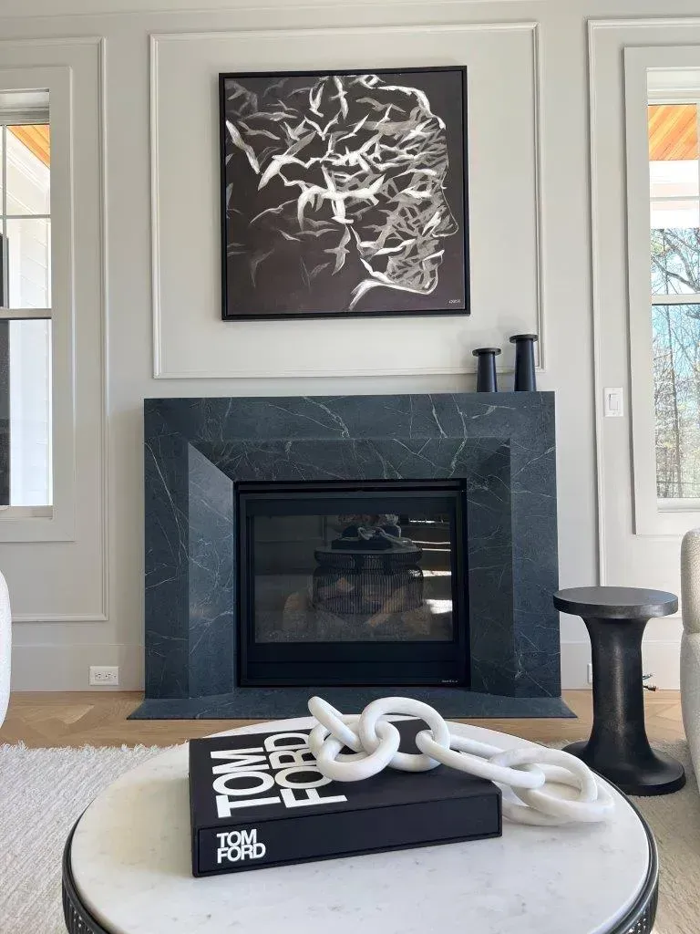 Modern fireplace with black mantel, abstract wall art, and a white sculptural decor piece on a coffee table