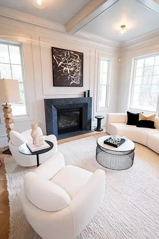 Bright white living room with fireplace, large windows, and modern cream chairs and ottoman.