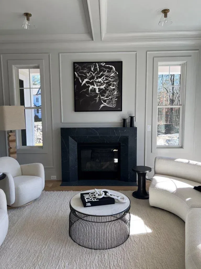 Elegant gray living room with black fireplace, abstract art, and white curved chairs around a round coffee table