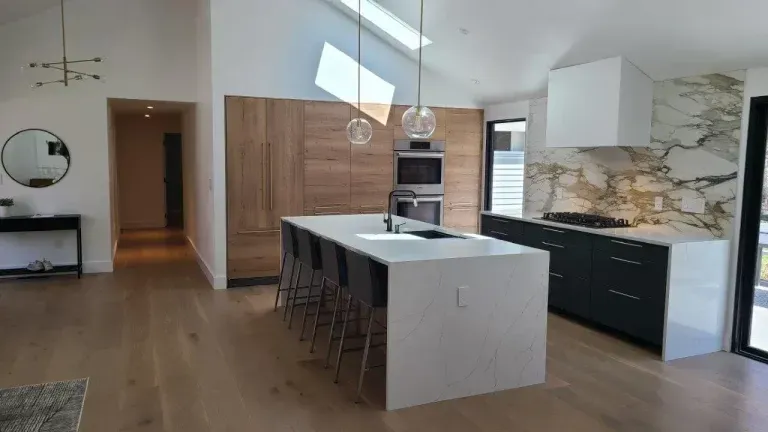 Modern kitchen with island, bar stools, pendant lights, dark cabinets, and wood floors