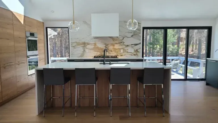 Modern kitchen with island, bar stools, wood cabinets, and sliding glass doors to a patio