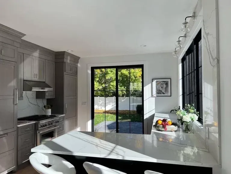 Modern kitchen with gray cabinets, marble island, and sliding glass doors to a patio.