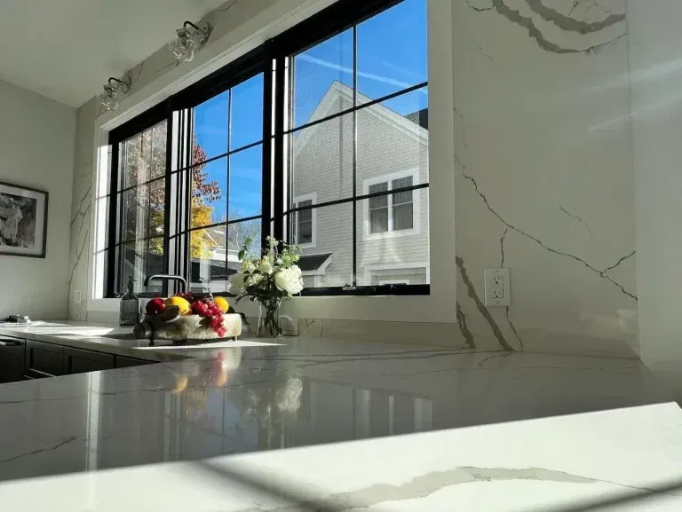 Bright kitchen with white marble counters, black-framed window, and fruit bowl in sunlight