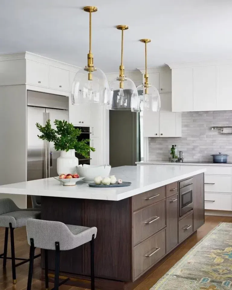 Modern kitchen with white cabinets, dark island, brass pendants, and gray stools