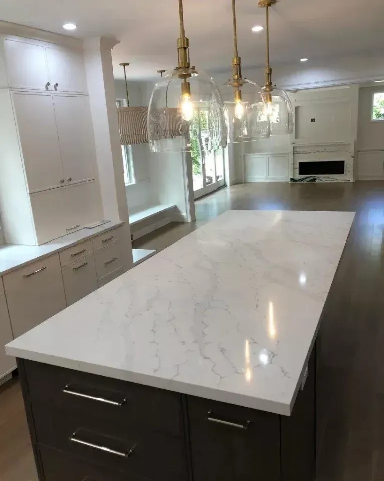 Modern kitchen with a large marble island, pendant lights, white cabinets, and a built-in fireplace