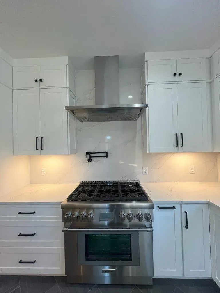 Modern white kitchen with stainless steel stove, range hood, cabinets, and warm under-cabinet lighting