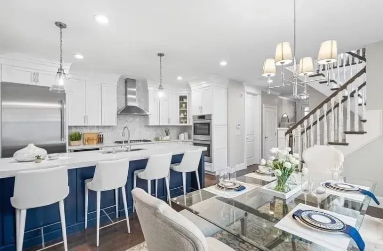 Bright white modern kitchen and dining area with island, bar stools, glass table, and staircase